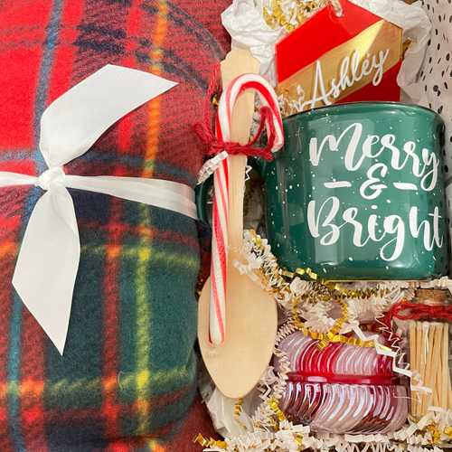 Red, green and blue fleece blanket, red and gold ornament, green mug reading merry & bright, candle, and matches